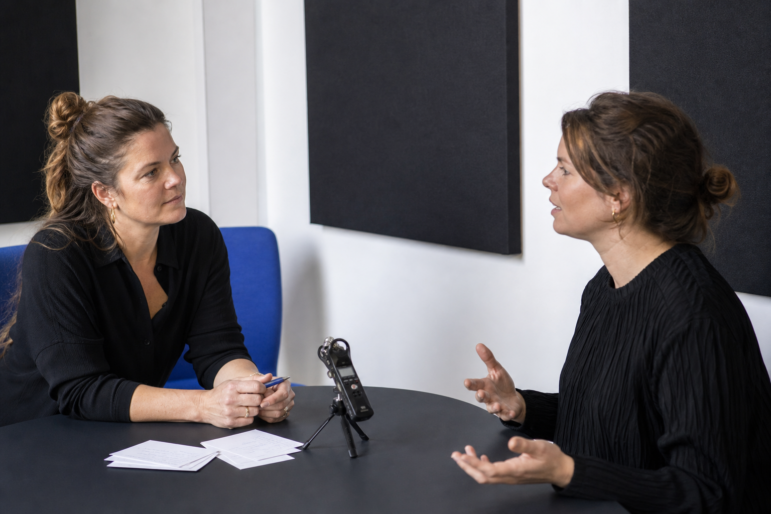 Twee collega's voeren een aandachtig gesprek met een audiorecorder op tafel
